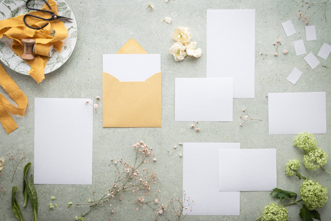 A flat lay of blank stationery and envelope amidst delicate flowers and ribbon, perfect for wedding or event planning.