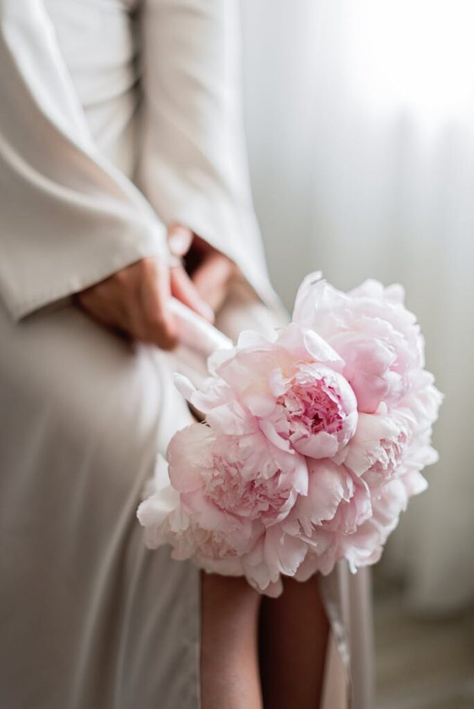 Close-up of a bride holding a bouquet of pink peonies, showcasing elegance and beauty.
